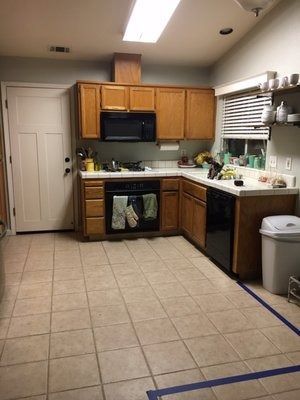 Small kitchen with wood cabinets, white countertops, tiled floor, and a door on the left.