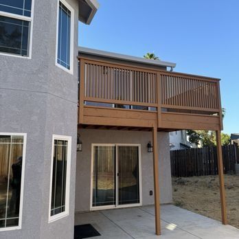 Backyard patio with covered wooden deck balcony and sliding glass doors on a gray house