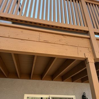 Wooden deck railing and underside of a raised porch against a beige house exterior