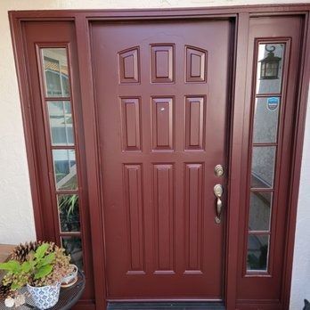 Maroon front door with sidelights and a potted plant by the entryway