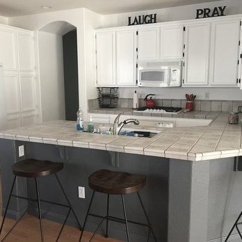 White kitchen with tiled island, two stools, and wall decor reading “LAUGH” and “PRAY.”