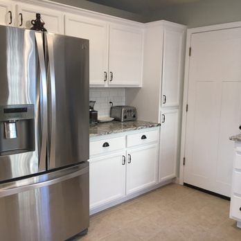 Bright white kitchen with stainless steel refrigerator, white cabinets, and beige floor near a pantry door