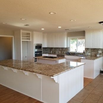 Bright modern kitchen with white cabinets, granite island, stainless appliances, and tiled floor