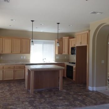 Empty kitchen with light wood cabinets, central island, pendant lights, and arched doorway.