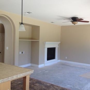 Empty beige living room with fireplace, ceiling fan, pendant light, and carpeted floor