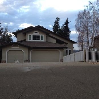 Suburban house with three garage doors, white fence, and cloudy sky at dusk
