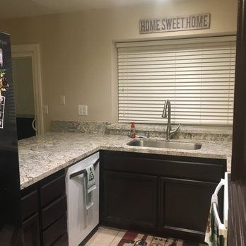 Kitchen corner with dark cabinets, speckled countertops, sink, and white blinds under a “Home Sweet Home” sign