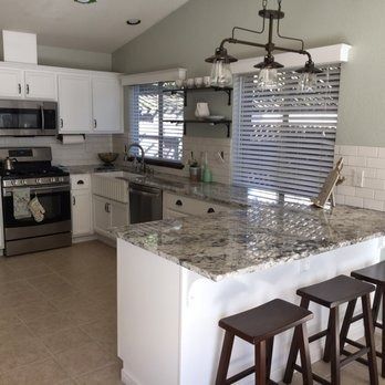 Bright modern kitchen with white cabinets, granite island, bar stools, and stainless steel appliances.