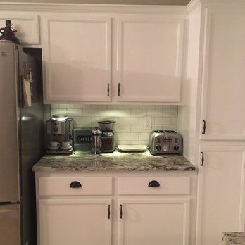 Small white kitchen with stainless fridge, coffee maker, toaster, and granite countertop above white cabinets