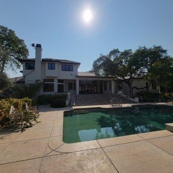 Sunny backyard with a two-story house and patio beside a swimming pool under a clear sky