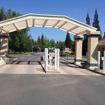 Gated park entrance with white metal archway, security barrier, and paved roadway under a clear blue sky