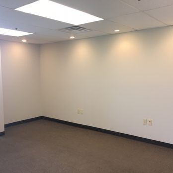 Empty office room with white walls, gray carpet, and recessed ceiling lights