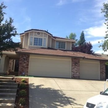 Suburban house with brick facade, two-car garage, and sunny driveway under a blue sky