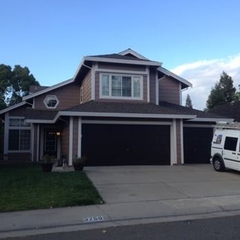 Two-story suburban house with a dark garage, driveway, and a white van parked at the curb.