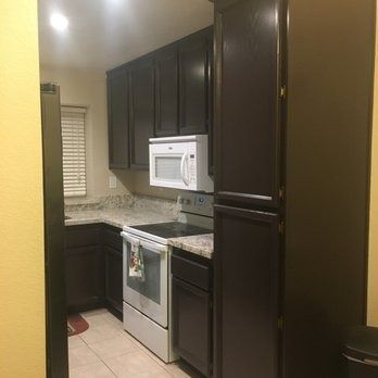 Narrow kitchen with dark cabinets, granite countertops, white appliances, and a small window.
