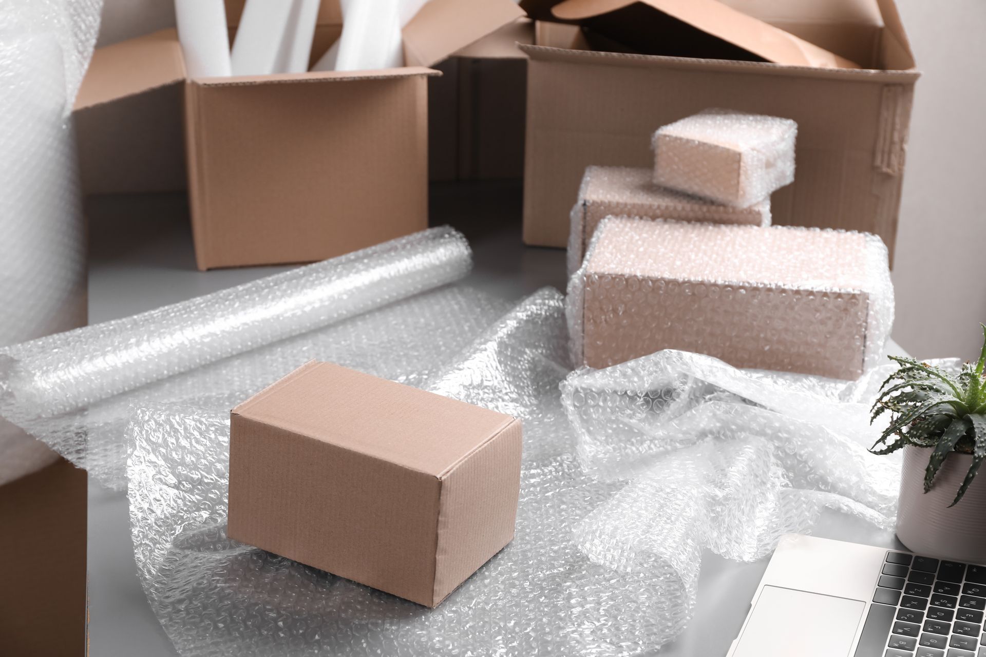 A table with a laptop, boxes, and bubble wrap in a warehouse.