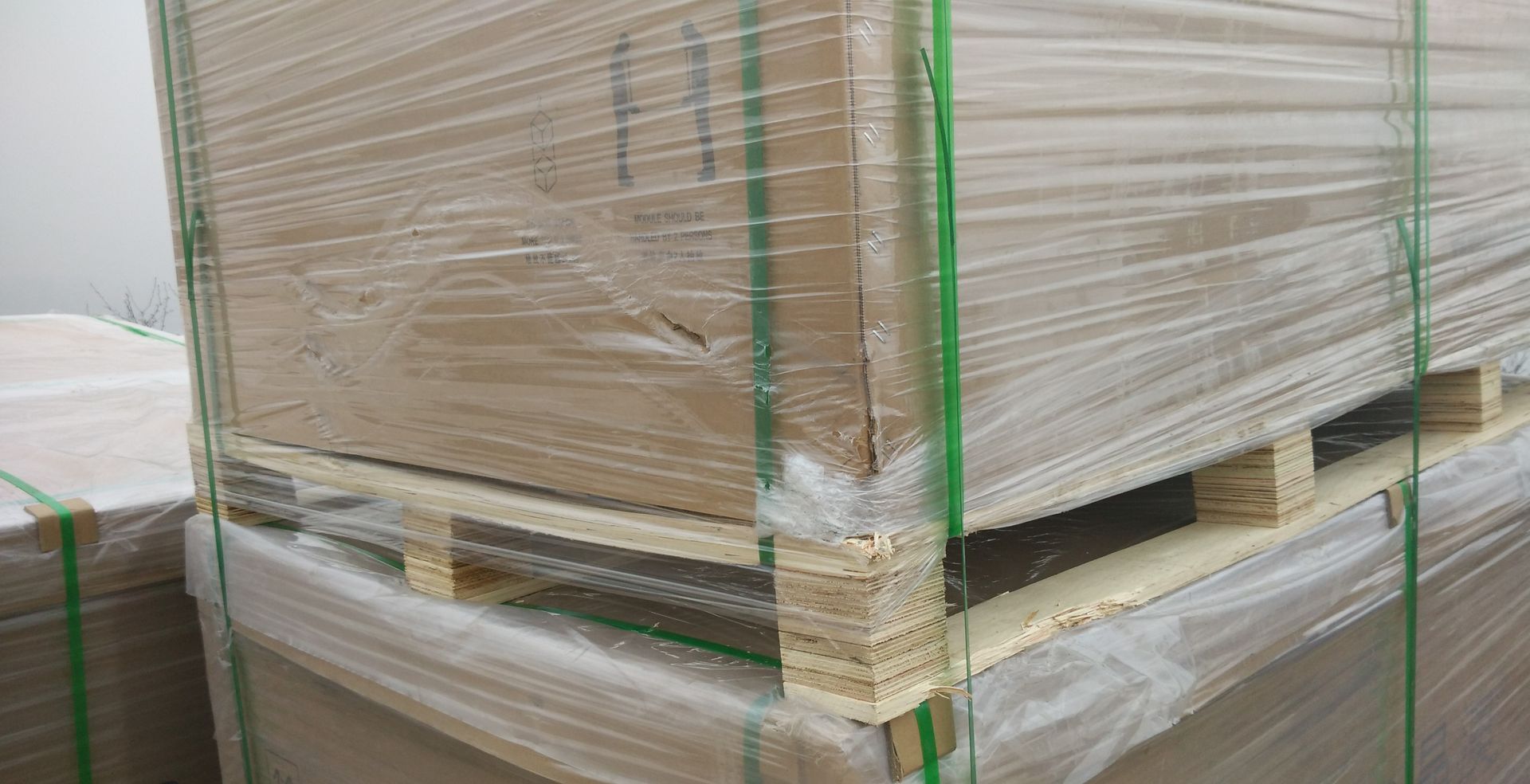 A stack of cardboard boxes wrapped in plastic on wooden pallets.