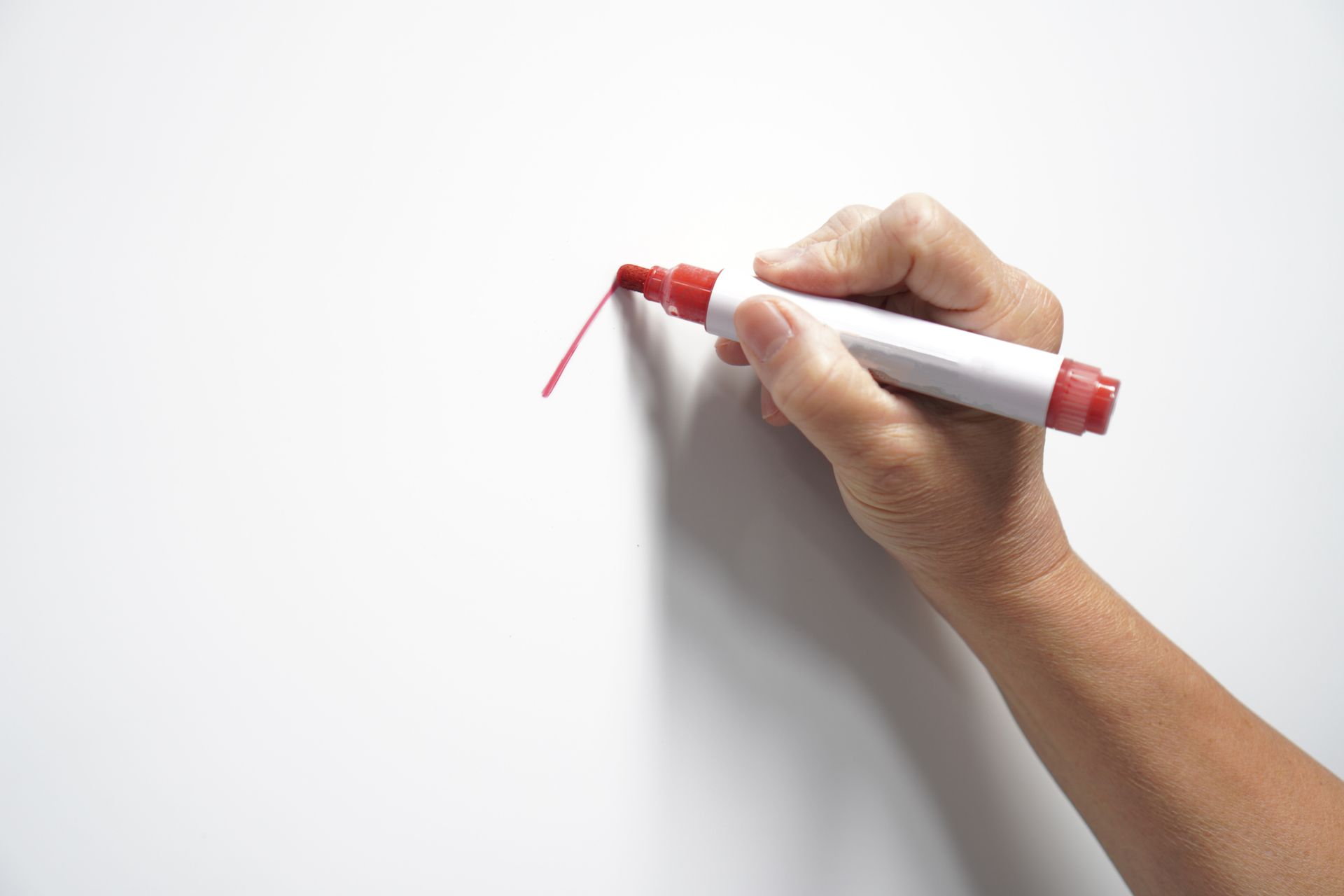 Hand holding a red marker, drawing a line on a white surface.