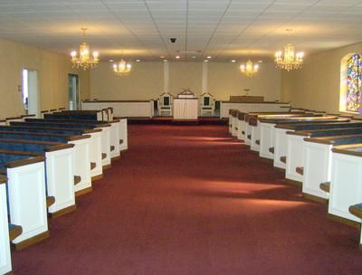 Empty church sanctuary with white pews, red carpet, chandeliers, and pulpit at the front