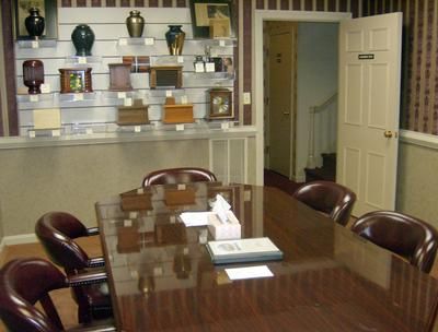 Conference room with a glossy wooden table, chairs, shelves, and an open doorway to a hallway.
