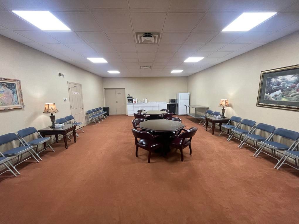 Empty community room with tables, blue chairs, beige walls, and overhead fluorescent lights