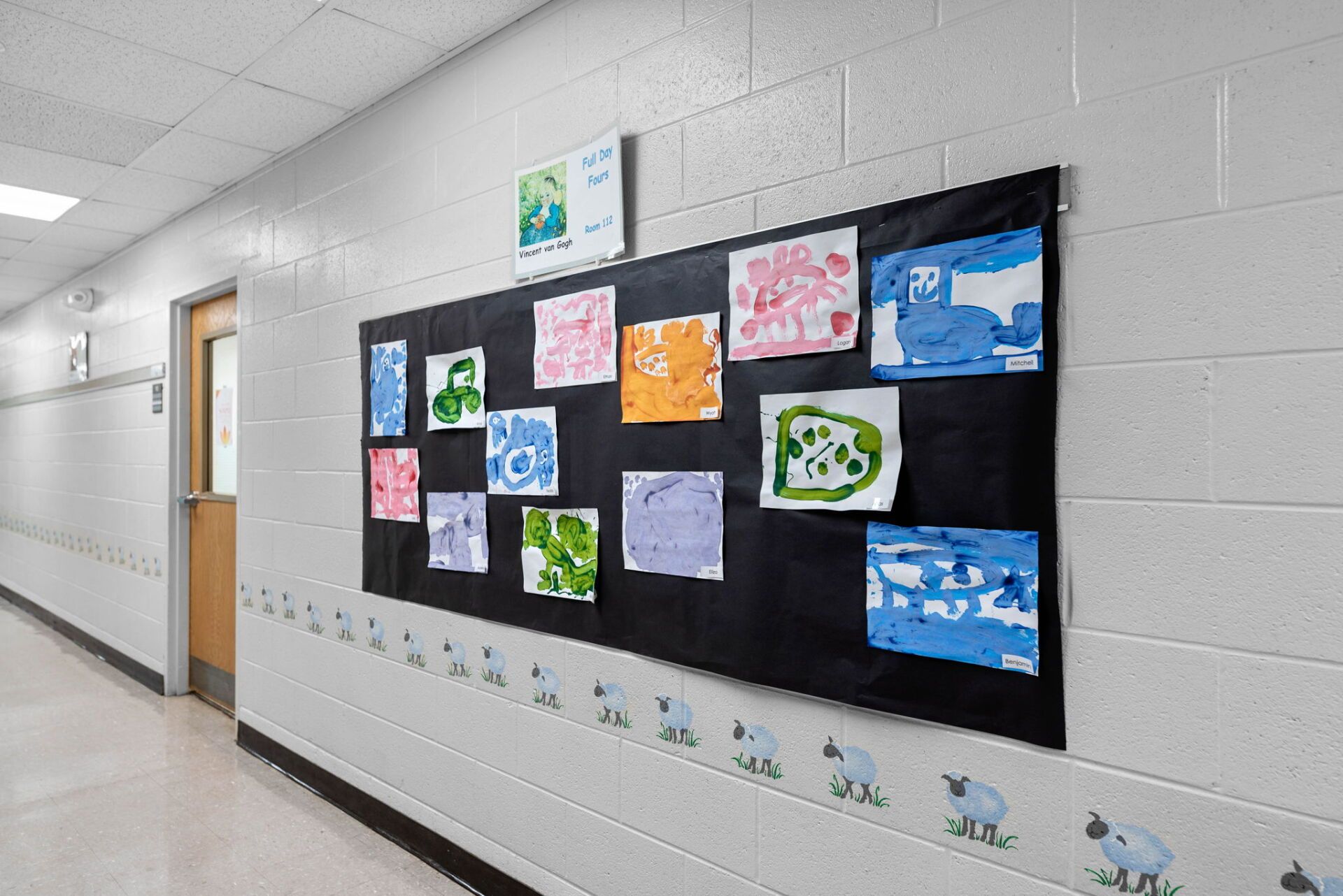 Hallway with white walls adorned with artwork and a border of sheep; a closed door is visible.