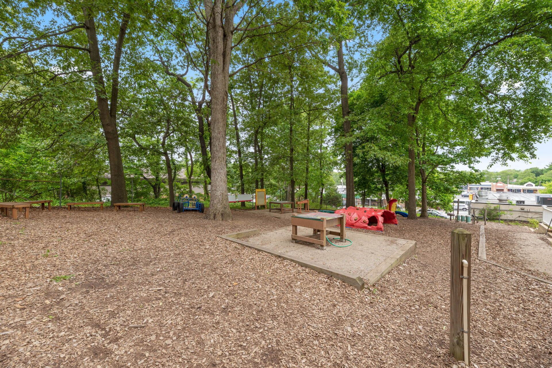 Playground with wood chips, a small table, and trees in a wooded area.