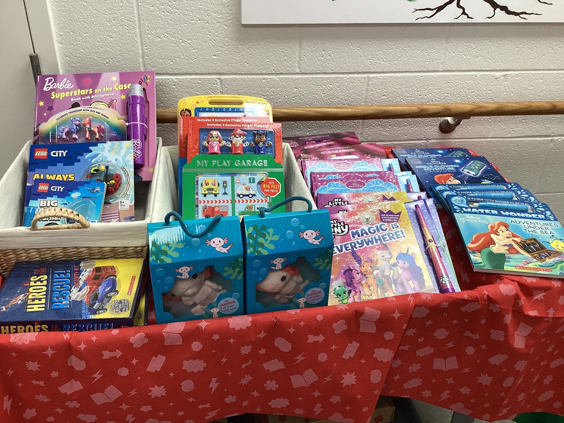 A table displaying various children's books and toys, including Paw Patrol gift bags, in a classroom or library setting.