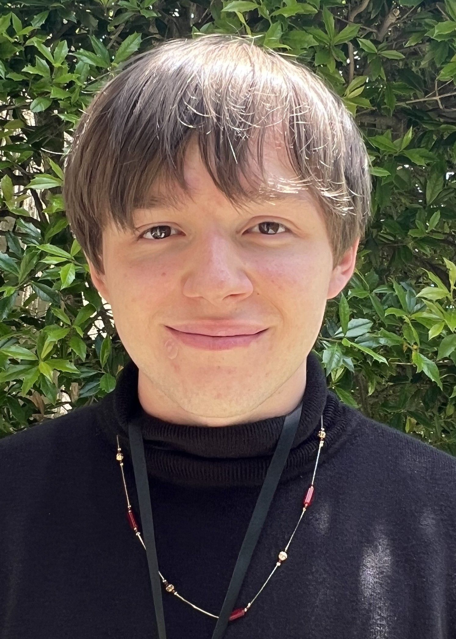 Woman with light brown hair wearing a fall-themed shirt and earrings, smiling at the camera outdoors.