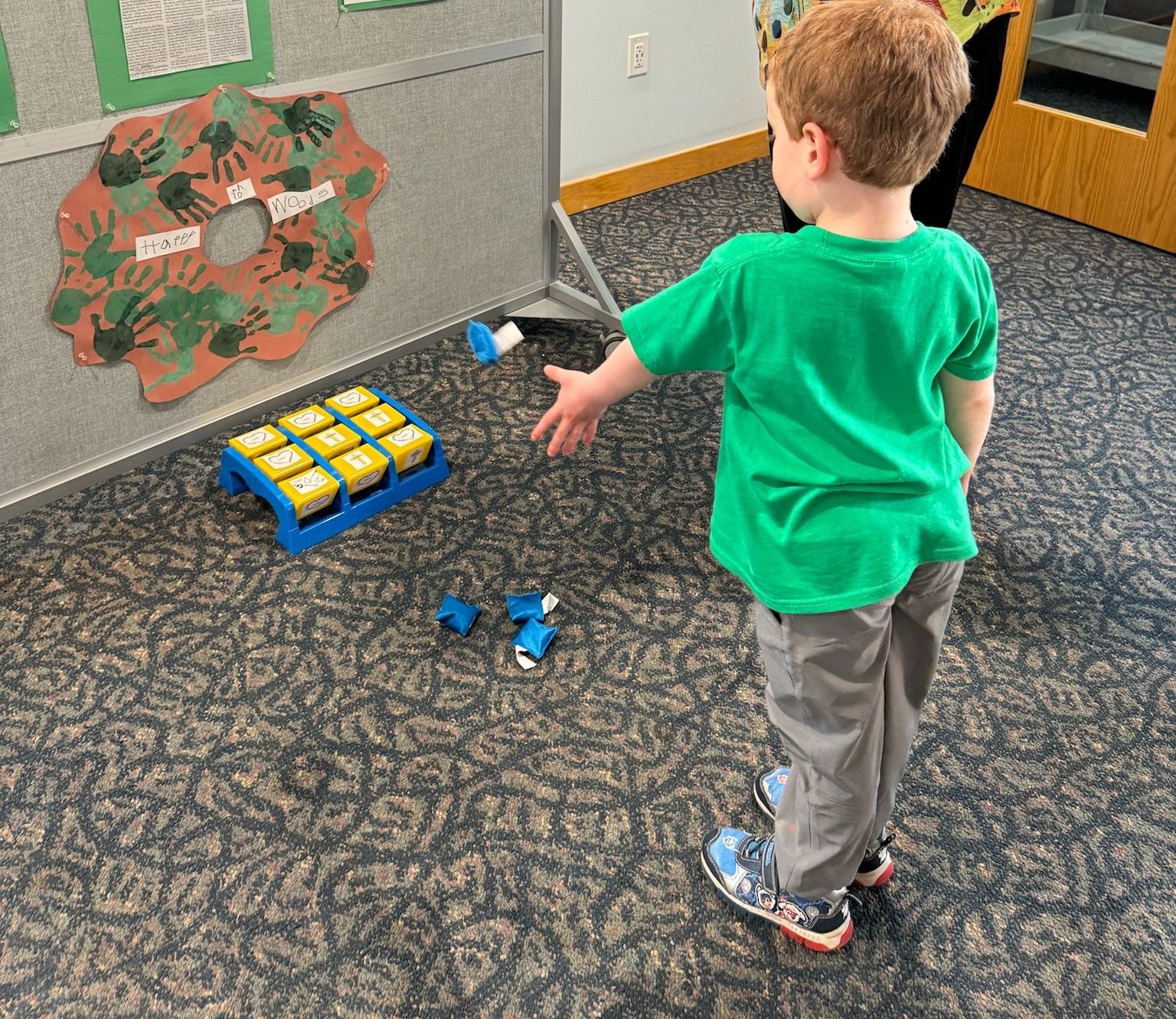 A young child in a green shirt throws a toy at a target game in a room.