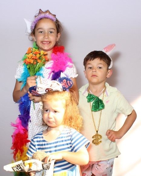 Three children in costumes. Girl in a crown and boa, boy with dollar sign necklace, and a younger girl with newspaper.