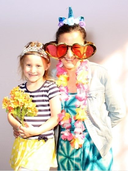 A woman and a young girl smile, dressed in costumes with a floral lei and flowers.
