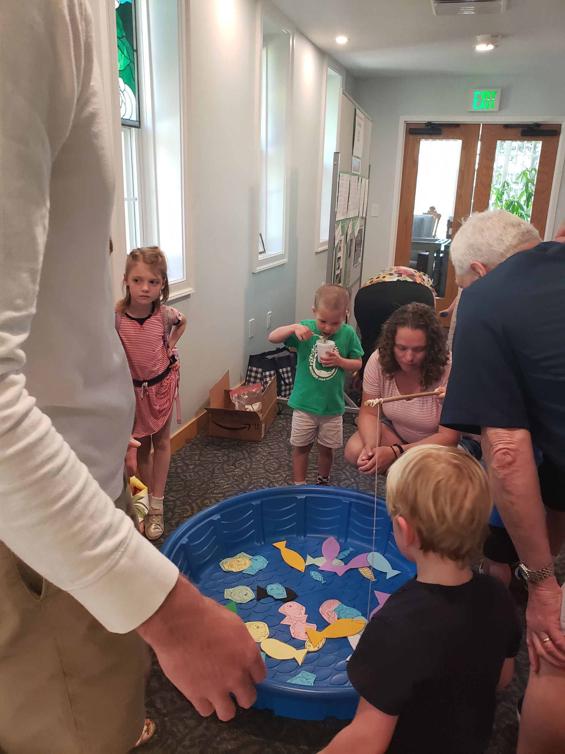 Children fishing in a blue plastic pool. Several kids and adults observe and participate indoors.