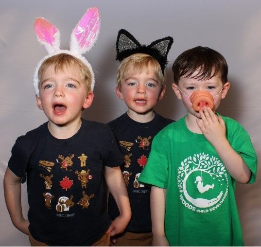 Three young children, wearing bunny ears, cat ears, and a pacifier, pose for a photo. They appear to be singing, with expressive faces.