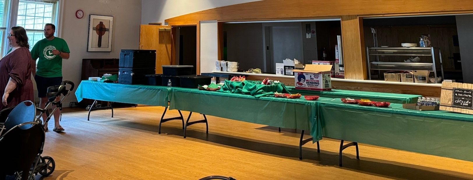 A person in a green shirt stands near a table covered in a green cloth, likely at an event inside a room.