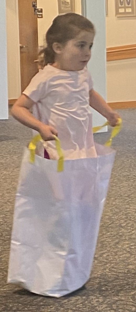 A young girl in a pink shirt inside a white sack, holding the handles and seemingly playing a sack race.