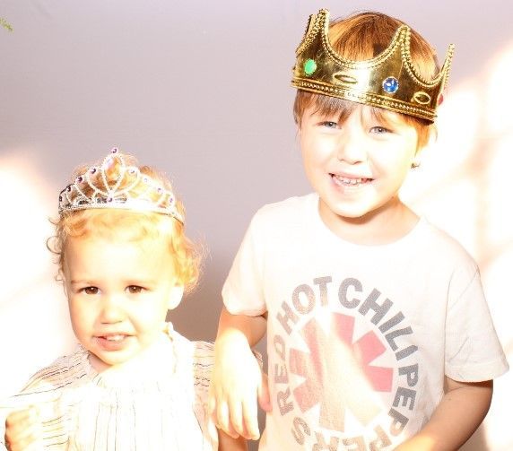 Two young children wearing crowns, the boy smiling in a Red Hot Chili Peppers shirt, the girl looking toward the left.