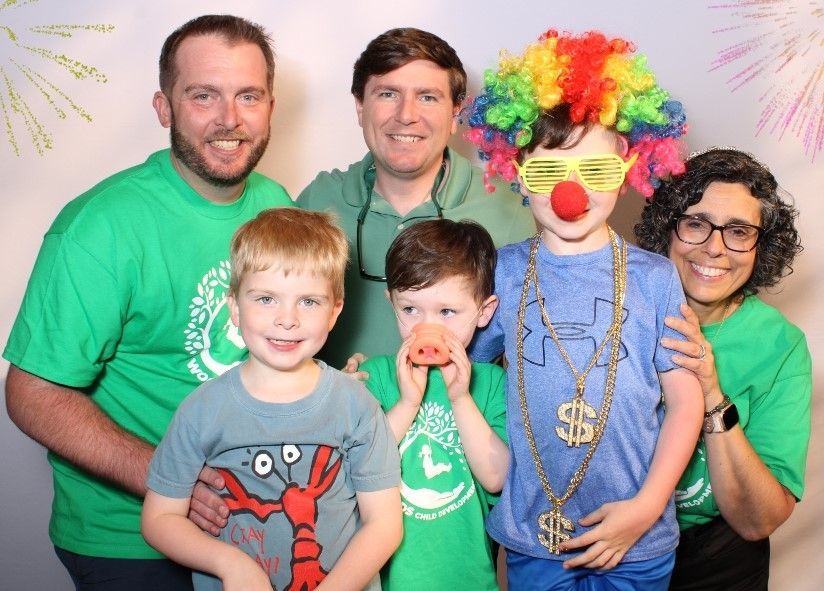 A group of people in a photo booth. Two adults, two children, and a person in a clown costume. Everyone is smiling.