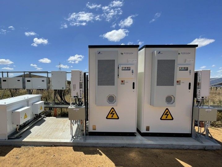 Two white power stations with warning signs, outdoors under a blue sky with clouds.