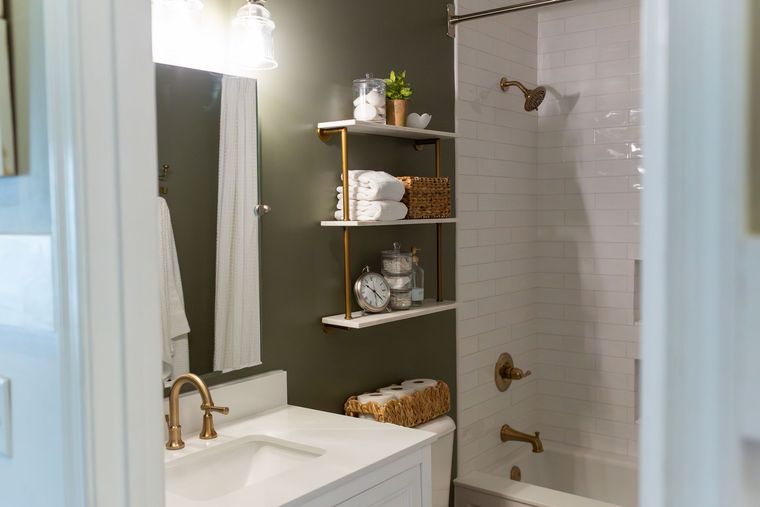 Bathroom vanity with sink, mirror, shelving, and a tiled shower with bronze fixtures.