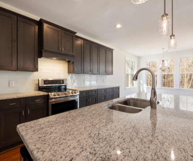 Modern kitchen with dark cabinets, granite island, stainless stove, and pendant lights