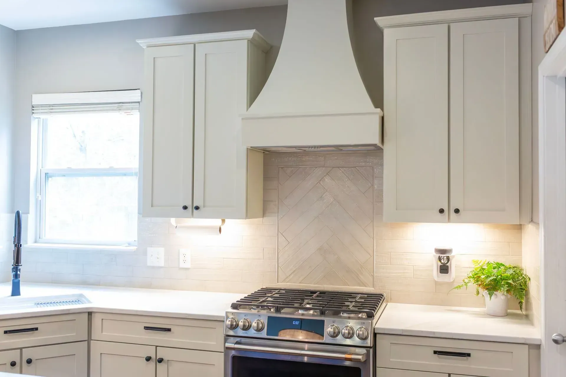 Bright white kitchen with gray cabinets, gas range, and tiled backsplash beneath a large hood