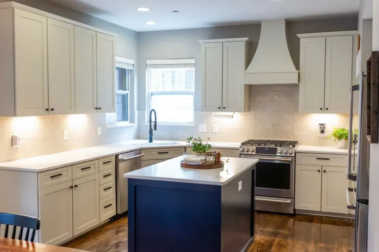 Bright, modern kitchen with white cabinets, navy island, stainless stove, and central island decor