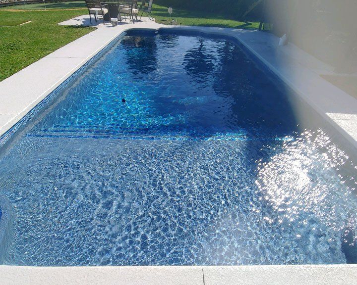 A large swimming pool is surrounded by grass and chairs