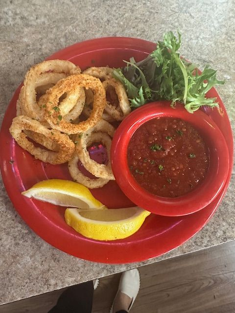 A plate of golden fried calamari rings served with a side of spicy dipping sauce, fresh greens, and lemon wedges.