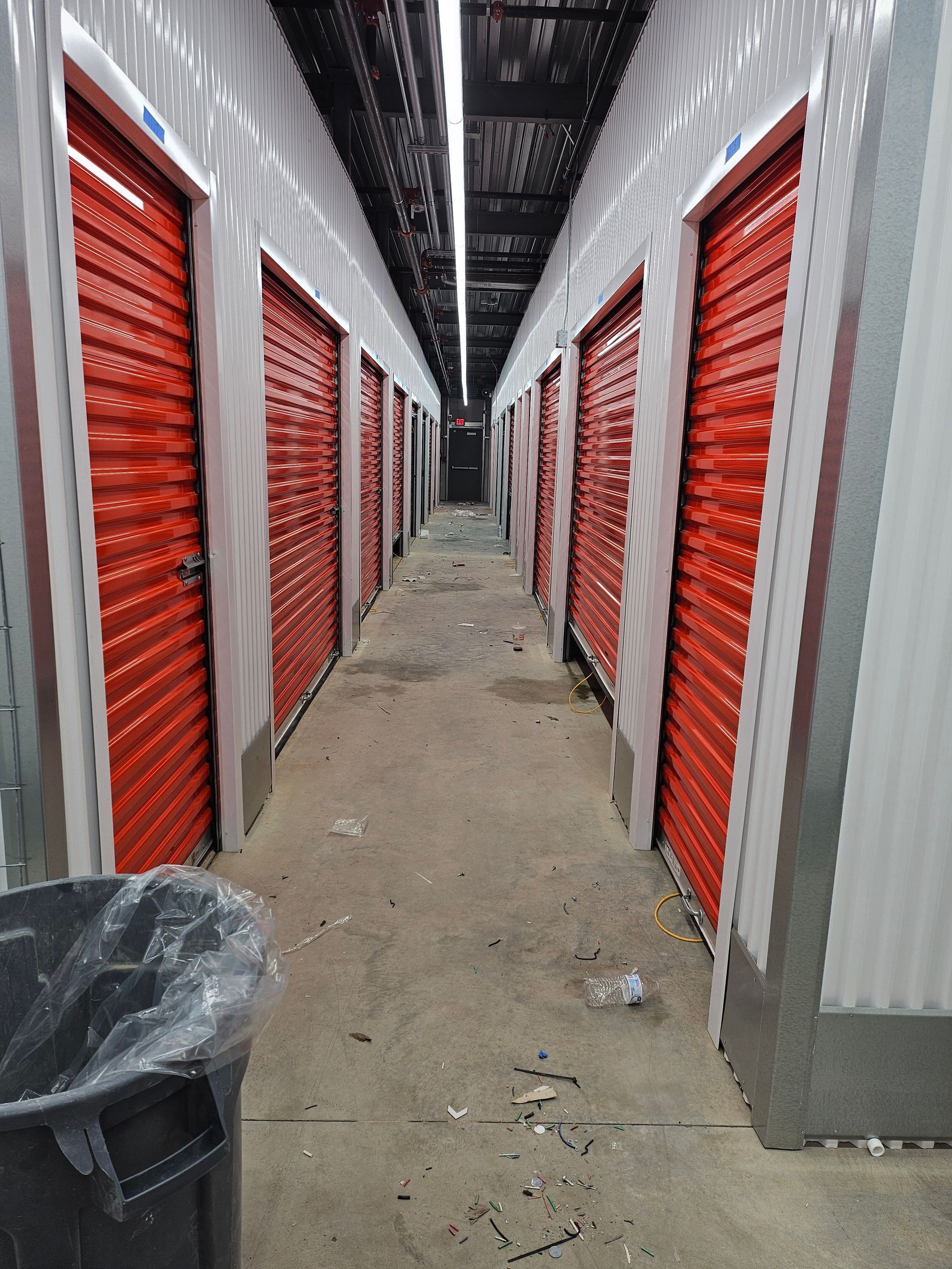 A long hallway with red doors and a trash can in the middle.