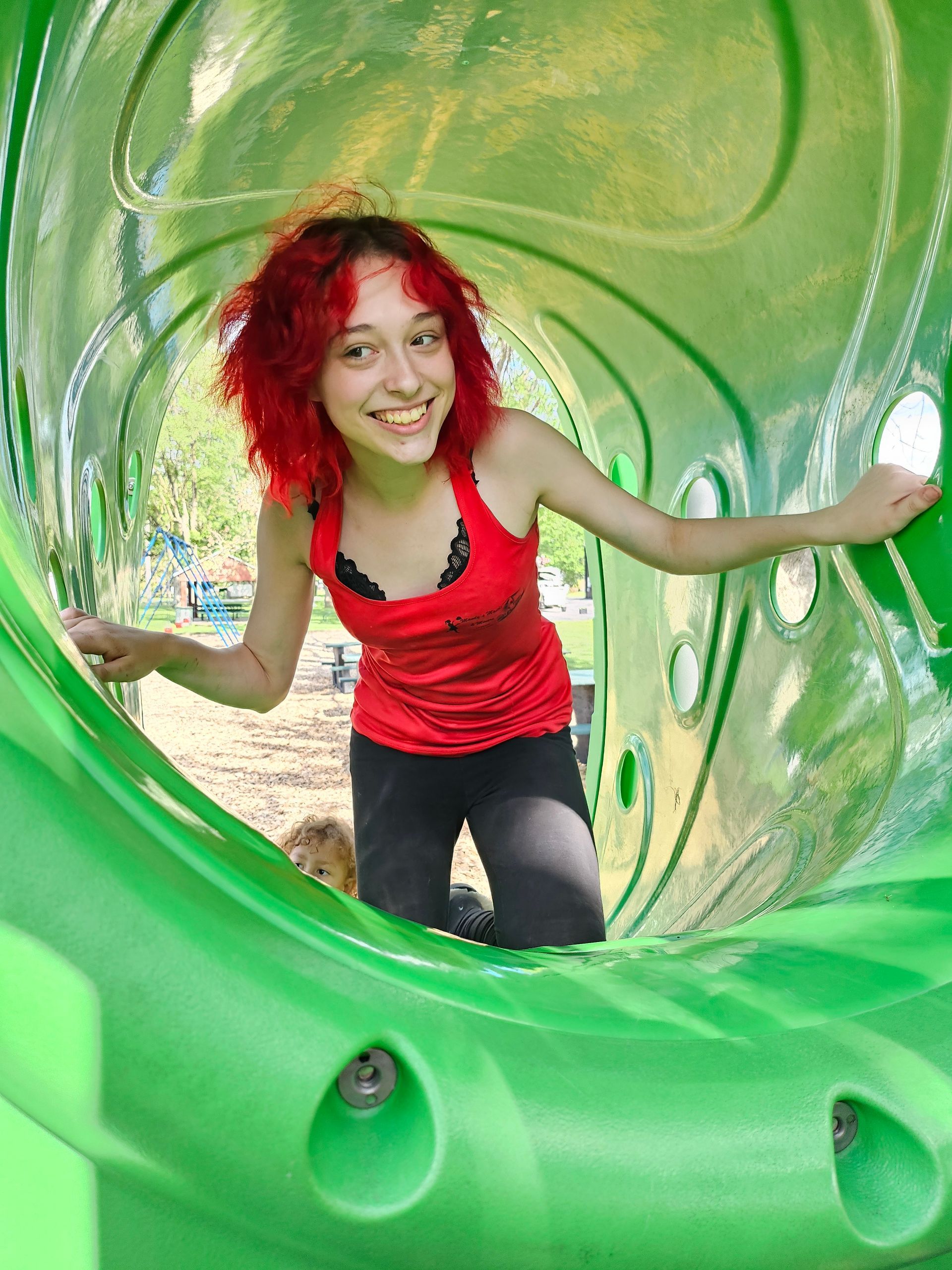 A girl with red hair is playing in a green tunnel