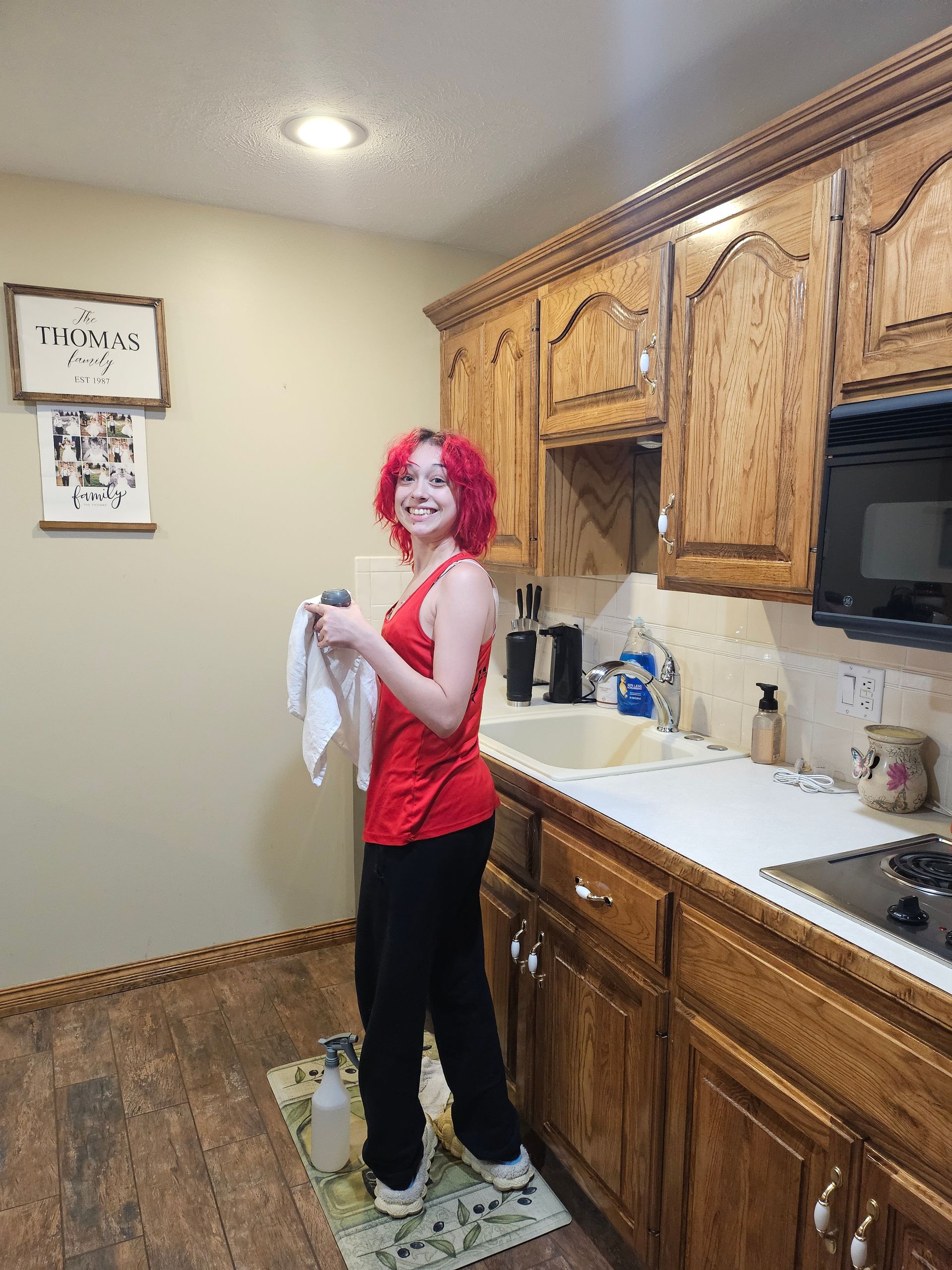 A woman with red hair is standing in a kitchen holding a towel.