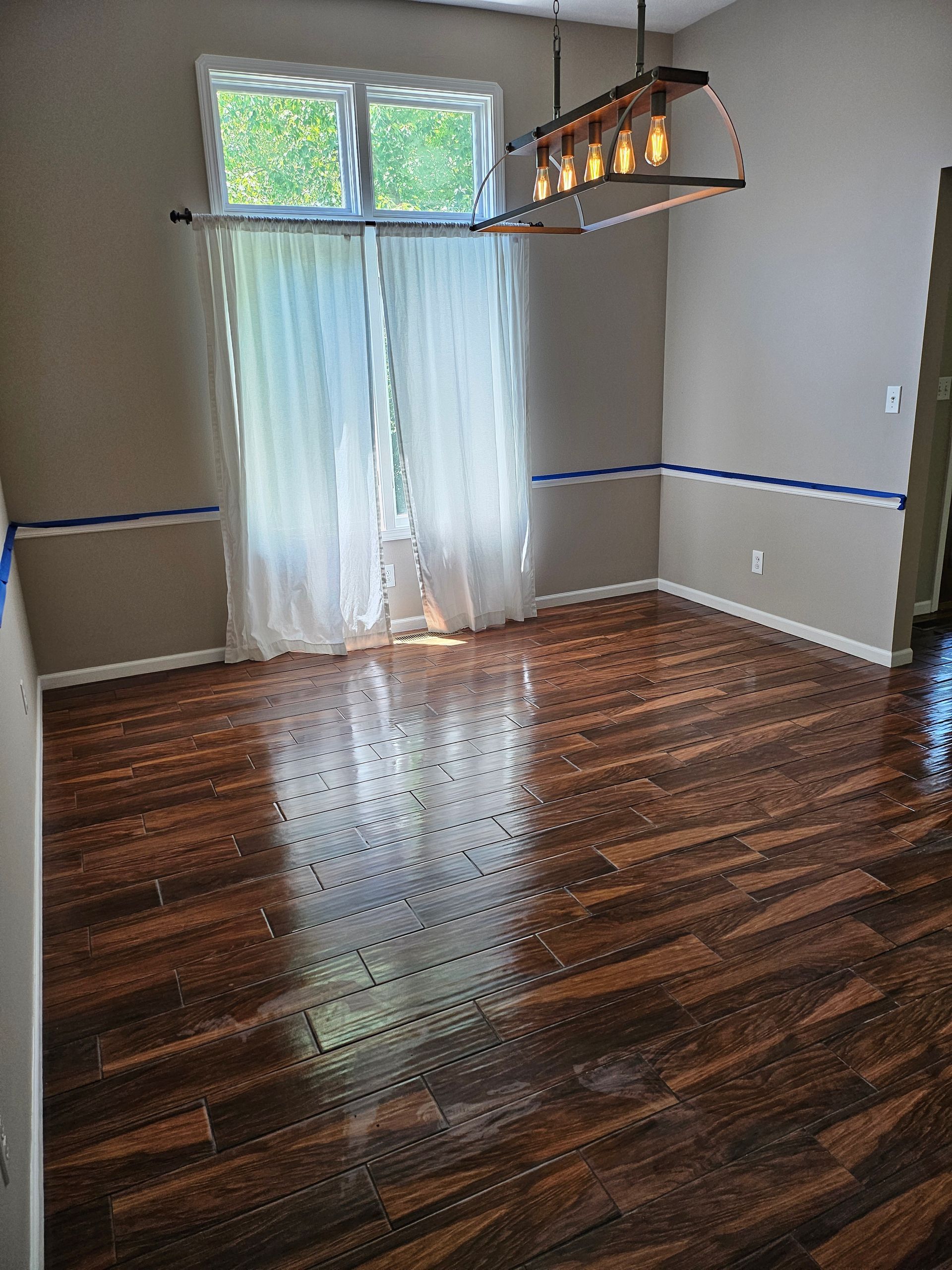 An empty dining room with hardwood floors and a chandelier hanging from the ceiling.