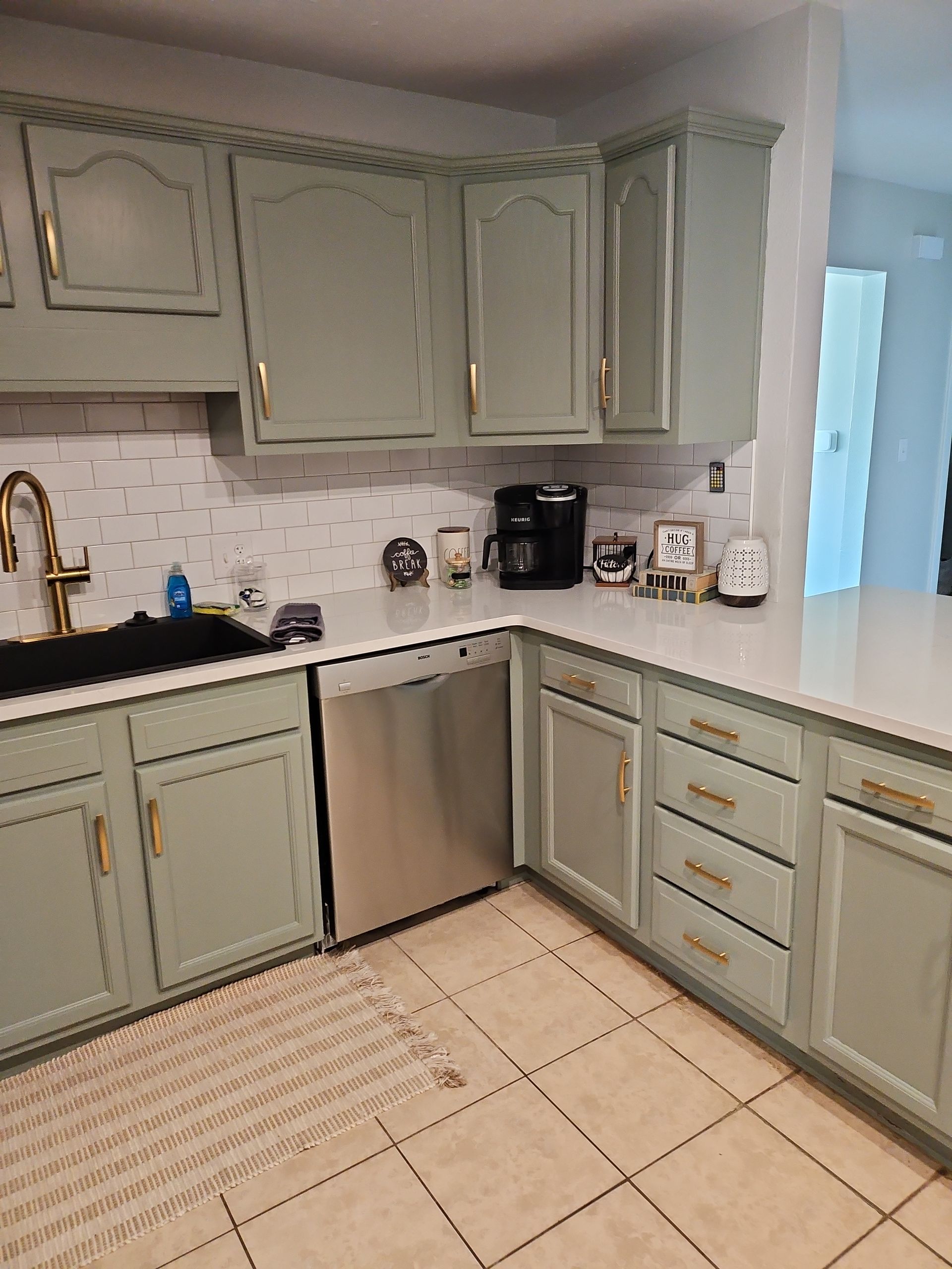 A kitchen with green cabinets , a sink , and a stainless steel dishwasher.